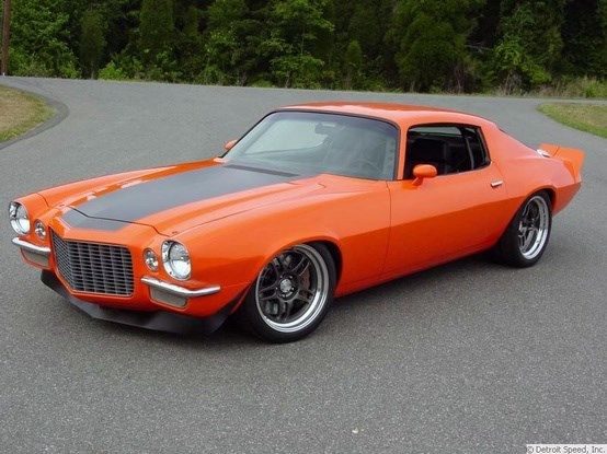 an orange muscle car parked on the side of a road next to a man wearing sunglasses