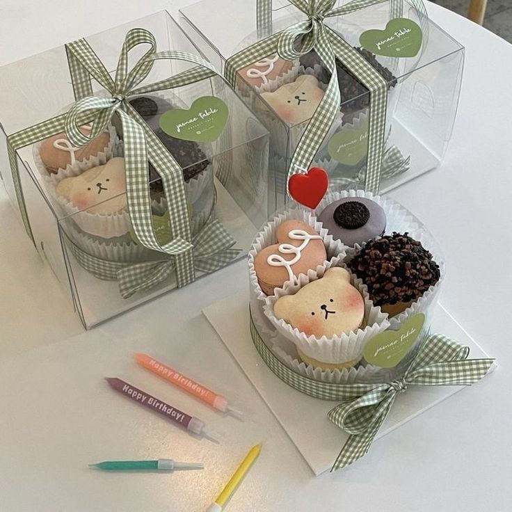 two clear boxes filled with cupcakes sitting on top of a table next to markers