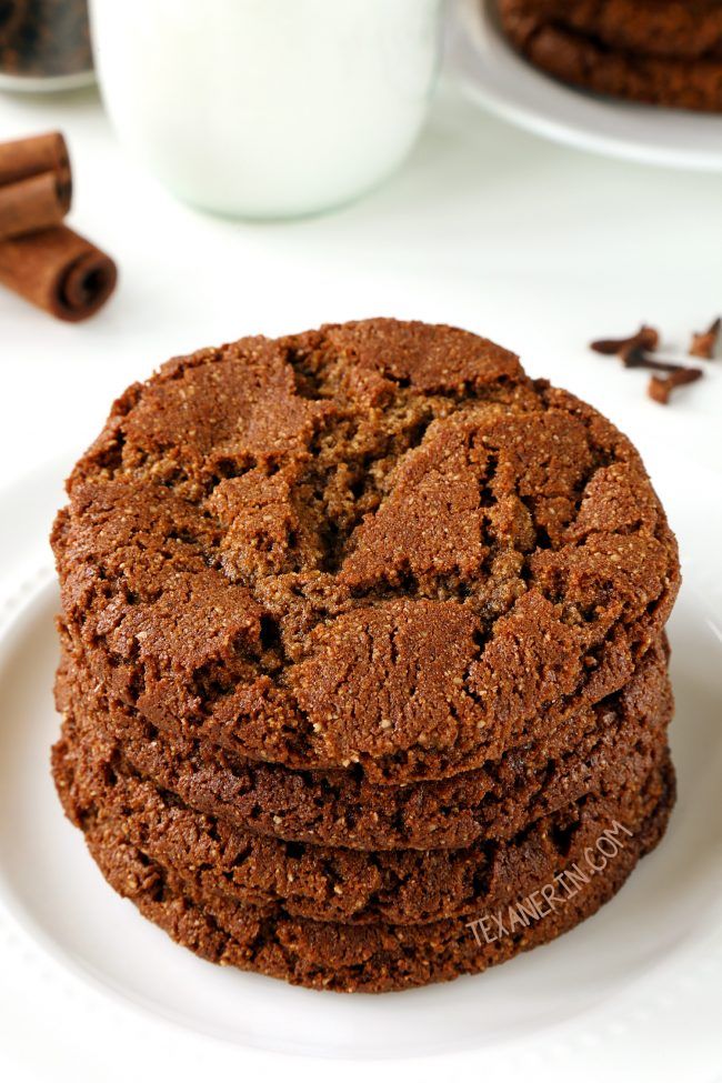 chocolate cookies stacked on top of each other with cinnamons in the foreground and milk in the background