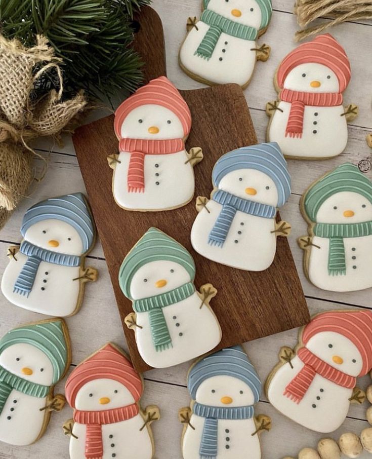 decorated cookies with snowmen and hats are on a wooden board next to pine cones