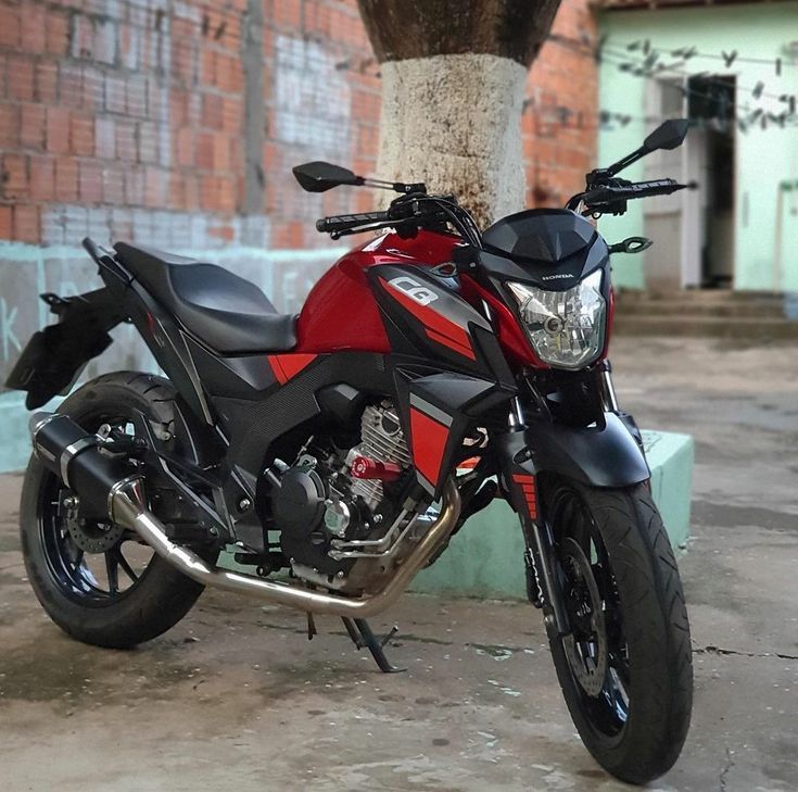 a red and black motorcycle parked next to a tree