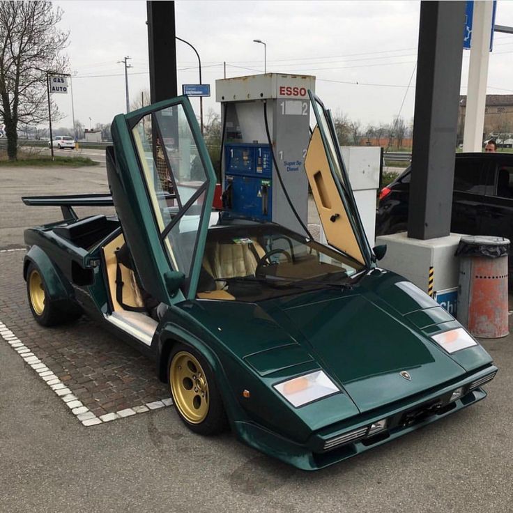 a green sports car parked at a gas station with its doors open and the hood up