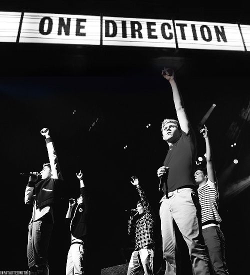 a group of young men standing on top of a stage under a one direction sign