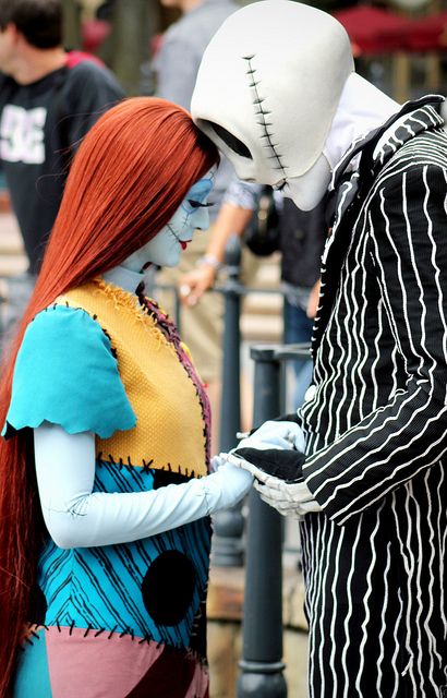 two people dressed in costumes standing next to each other on a street corner, one with long red hair and the other with blue eyes