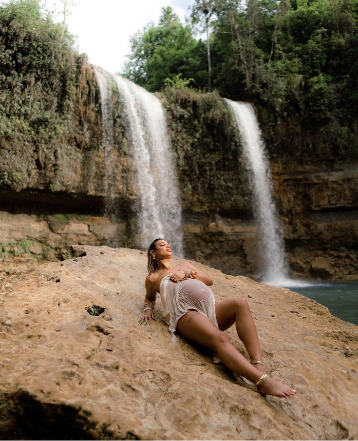 a woman laying on top of a rock next to a waterfall