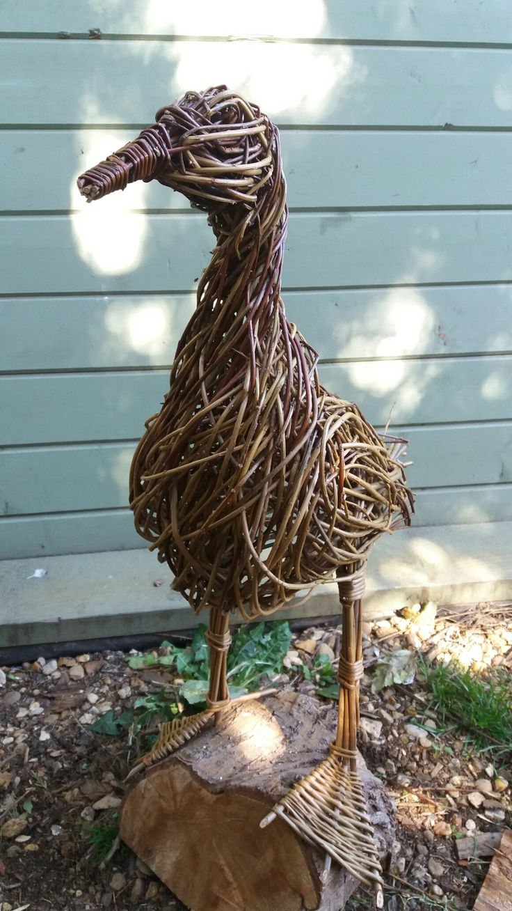 a sculpture of a bird made out of twigs on top of a tree stump in front of a house