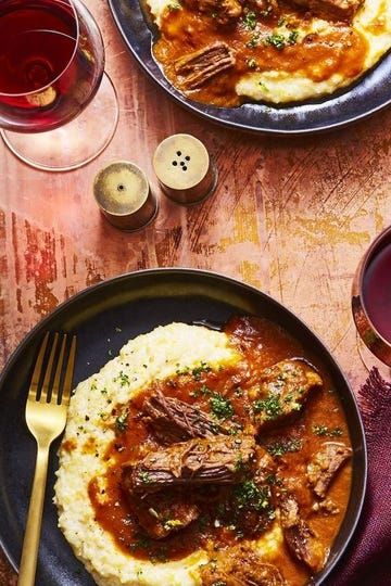 two plates of food with meat and mashed potatoes on the table next to wine glasses