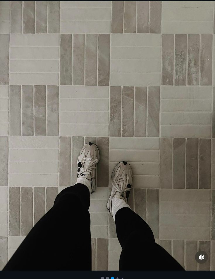 a person standing on a tile floor with their feet propped up against the wall and wearing white sneakers