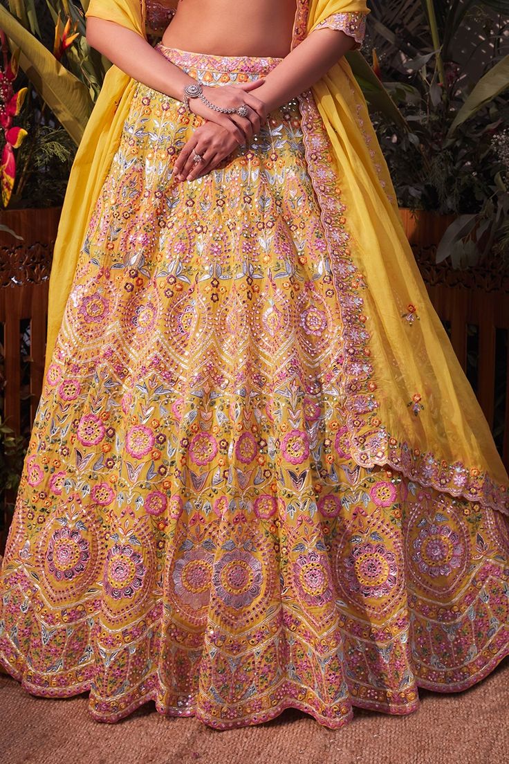 Yellow lehenga with mirror work, multicolor thread embroidery and gota patti trims. Comes with blouse and dupatta.
Component: 3
Pattern: Embroidery
Type Of Work: Mirror, Thread, Foil and Gota Patti
Neckline: V neck
Sleeve Type: Sleeveless
Fabric: Organza
Color: Yellow
Other Details: 
Scalloped detail on the neckline and hem
Dupatta with embroidery and scalloped border
Closure: Hook front
Note: Pink lehenga worn by the other model is not for sale
Occasion: Bride - Aza Fashions Lehenga With Mirror Work, Yellow Mirror, Embroidery Mirror, Organza Embroidery, Yellow Lehenga, Scalloped Border, Pink Lehenga, Luxury Sale, Pattern Embroidery