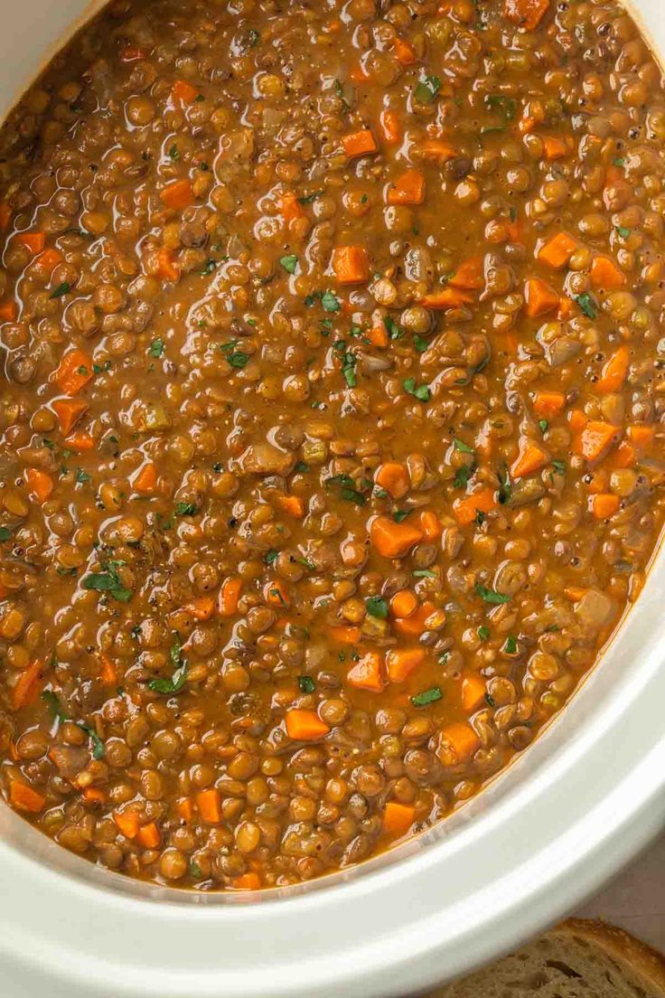 a white crock pot filled with lentils and carrots next to a slice of bread