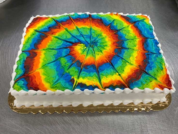 a rainbow cake with white frosting and icing on a silver tableclothed surface