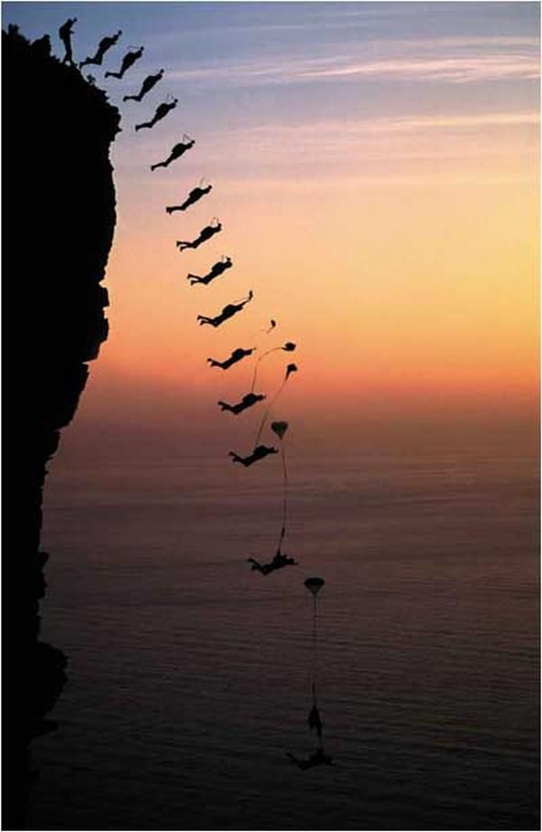 a long line of birds flying over the ocean at sunset