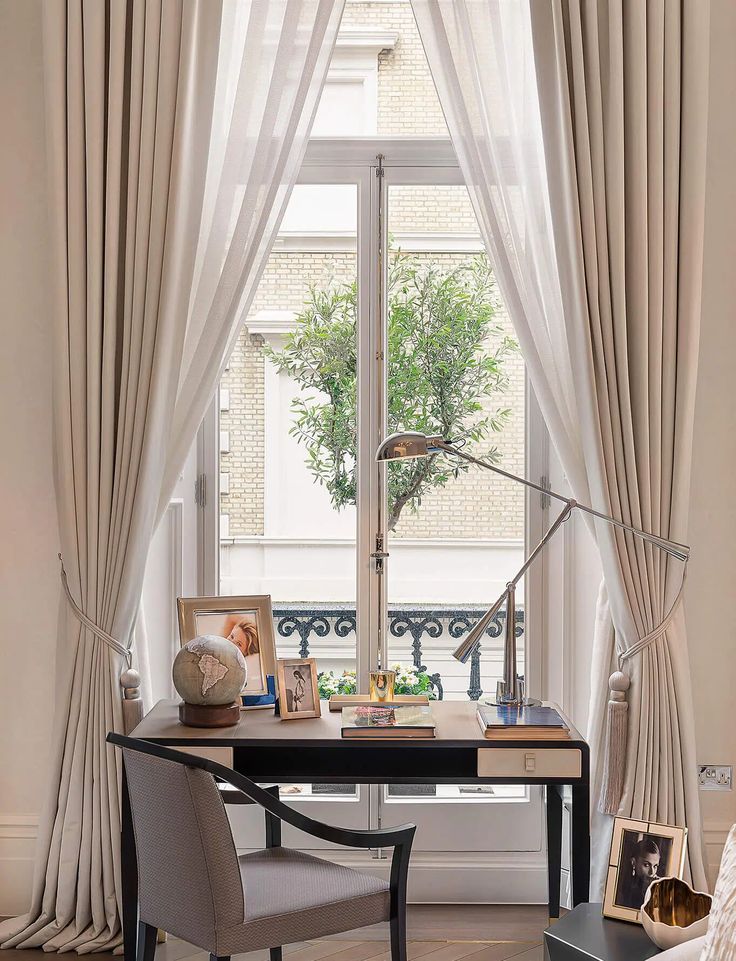 a bedroom with a desk and chair in front of a window that has drapes on the windowsill