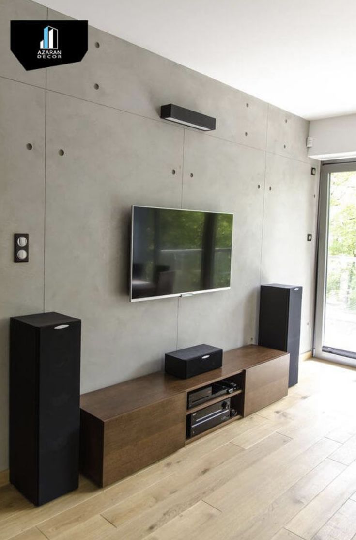 an entertainment center with two speakers and a flat screen tv mounted on the wall, in front of a sliding glass door