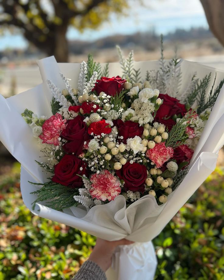 a bouquet of red and white flowers in someone's hand