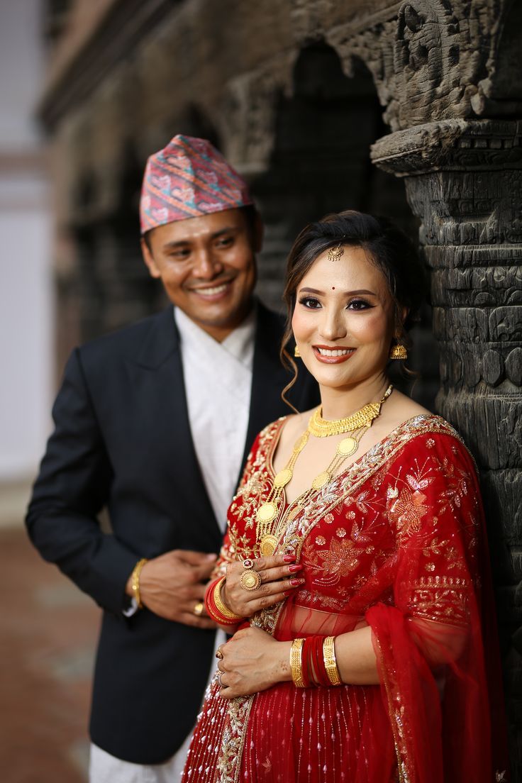 a man standing next to a woman wearing a red sari and smiling at the camera