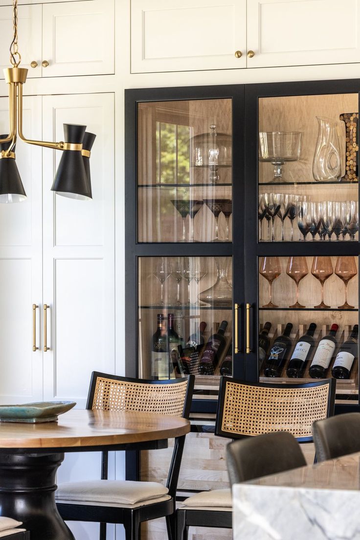 a dining room table and chairs with wine glasses on display behind them in a cabinet