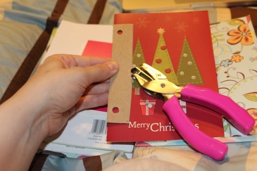 a person holding a pair of pink scissors next to christmas cards and envelopes on a bed