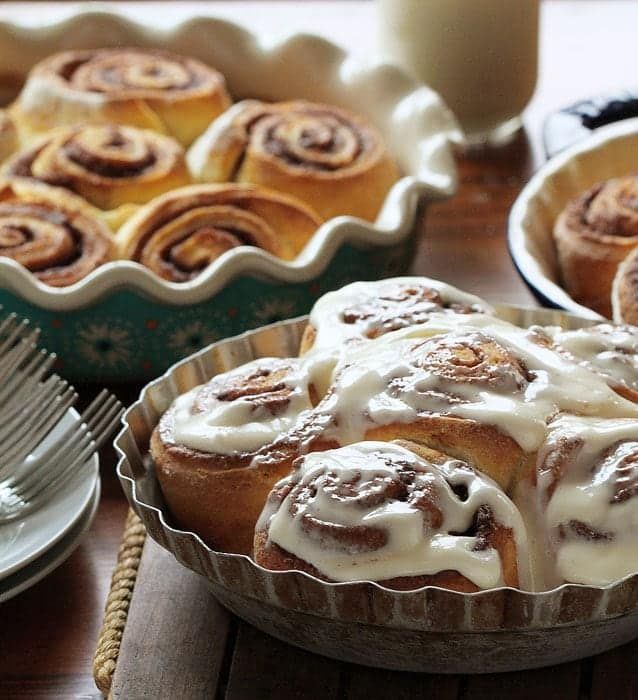 cinnamon rolls are sitting in pans on a table with plates and utensils