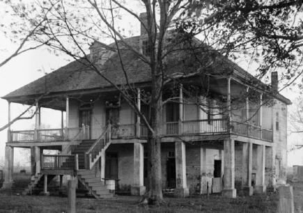 an old house sitting in the middle of a field next to a fence and trees