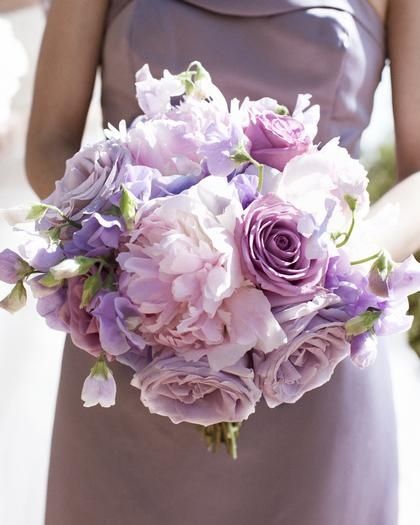 a bridesmaid holding a bouquet of purple flowers and greenery in her hand