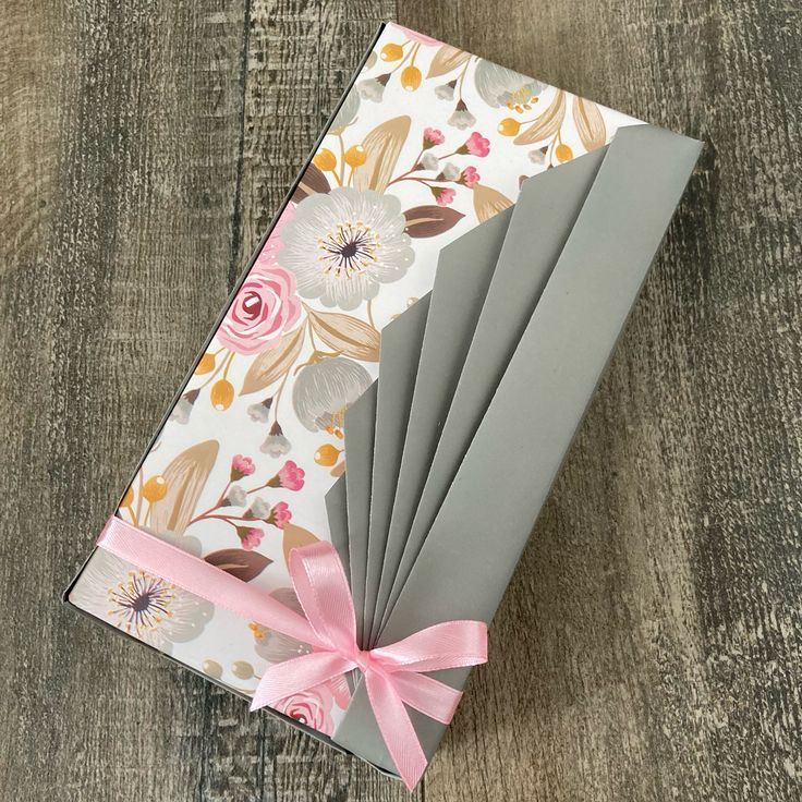 six folded cards with pink ribbon tied around them on top of a wooden table next to a pair of scissors