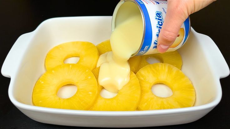 a person pouring sauce on top of sliced pineapples in a white bowl with two slices