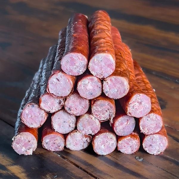 several sausages stacked on top of each other in front of a pile of sticks