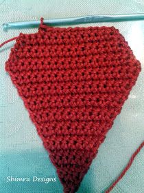 a red crocheted triangle sitting on top of a table next to a knitting needle