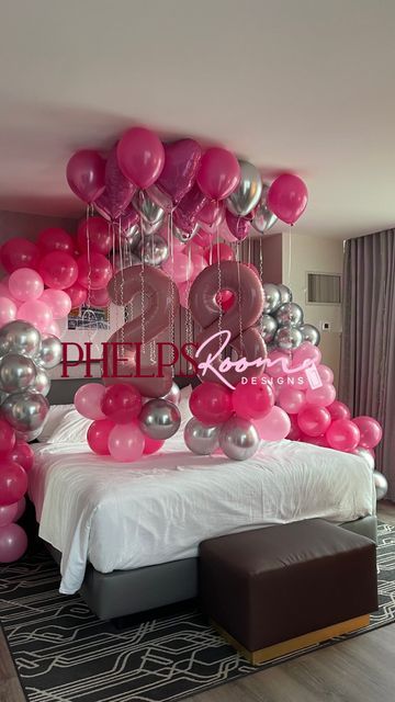 pink and silver balloons are hanging from the ceiling above a bed in a hotel room