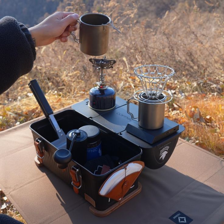 a person holding a cup over an outdoor stove