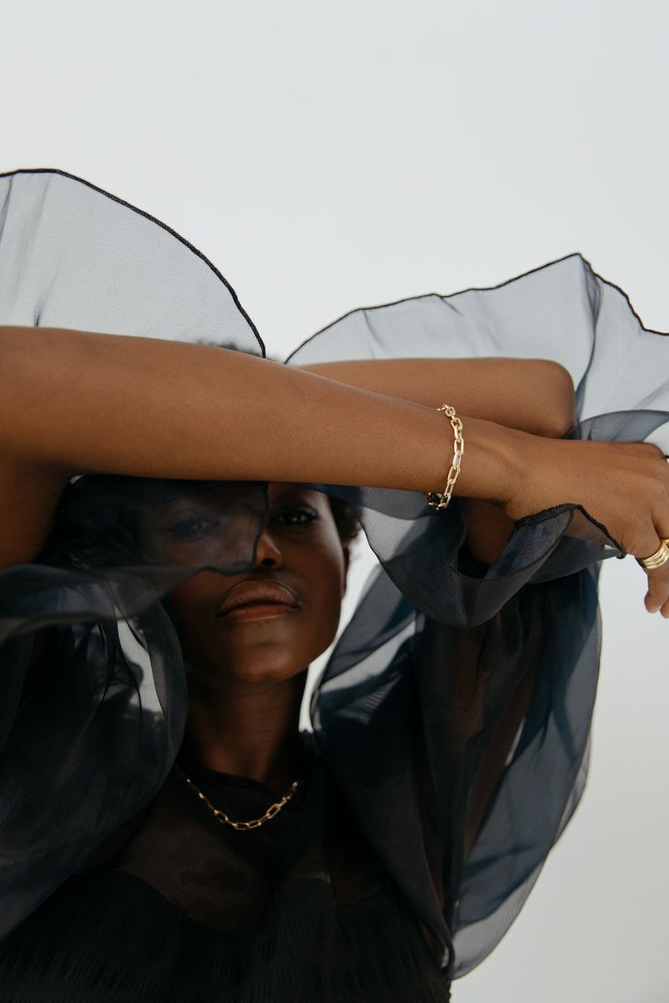 a woman with her hands on her head and wearing a black shirt, gold bracelets