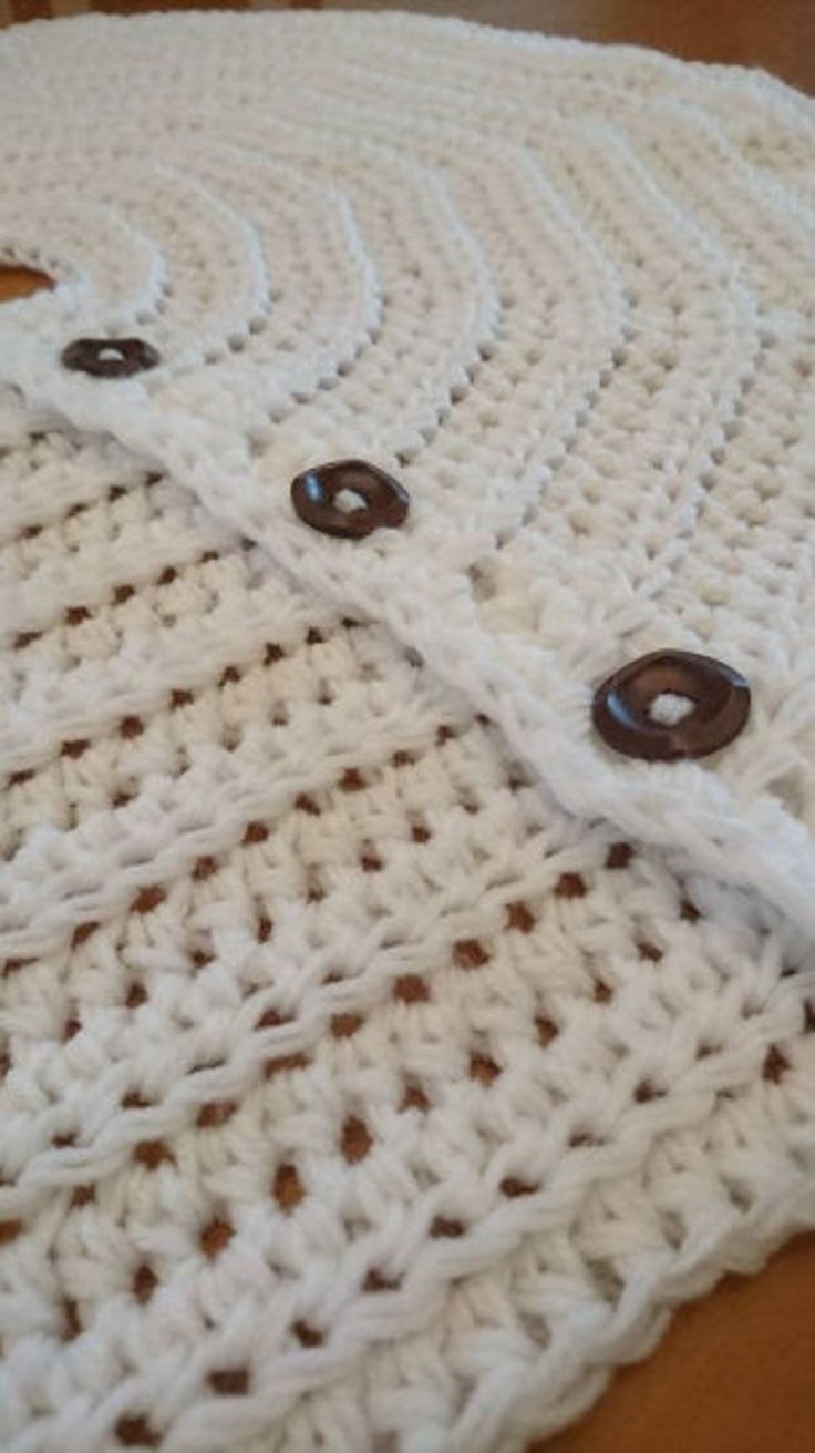 a crocheted white blanket with buttons on the bottom and brown buttons in the middle