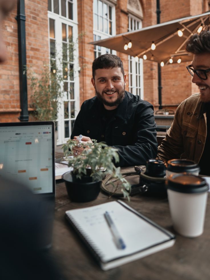 three men sitting at a table with laptops and coffee cups in front of them