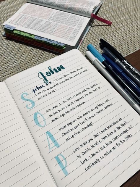 an open book with writing on it next to two pens and a notebook that has the word john written in blue ink