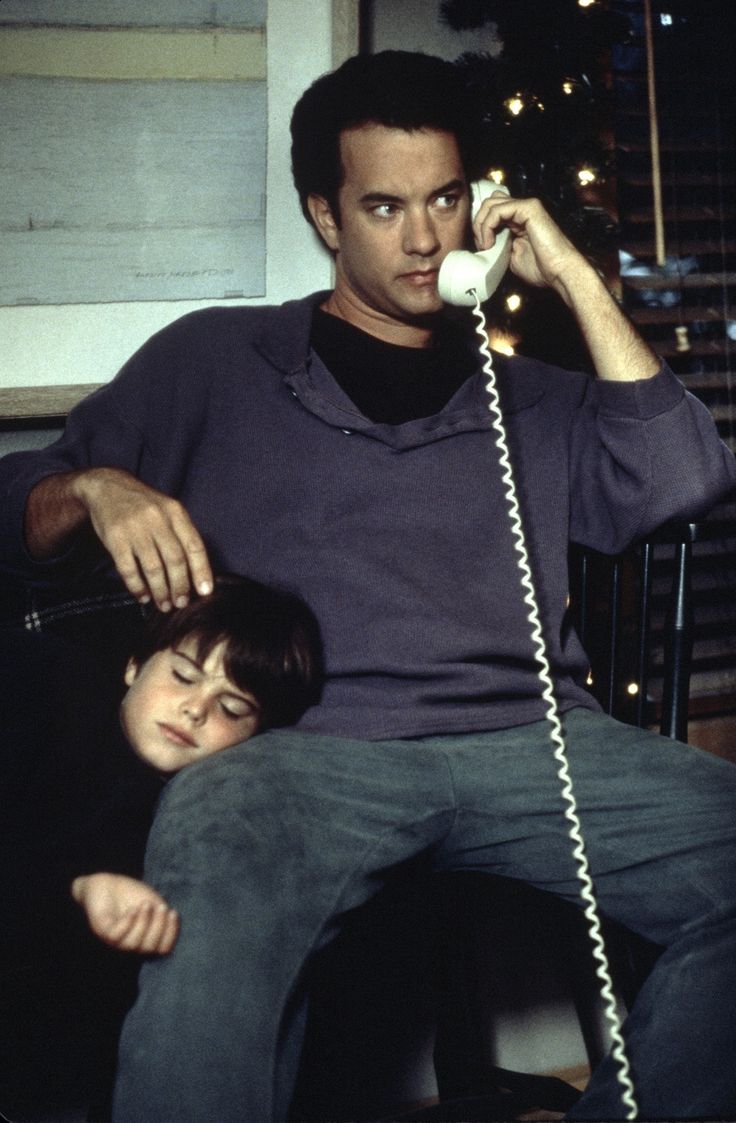 a man sitting in a chair while talking on a phone next to a young boy