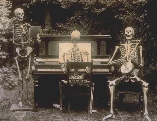 two skeletons sitting at a piano in front of a tree and another skeleton standing next to it