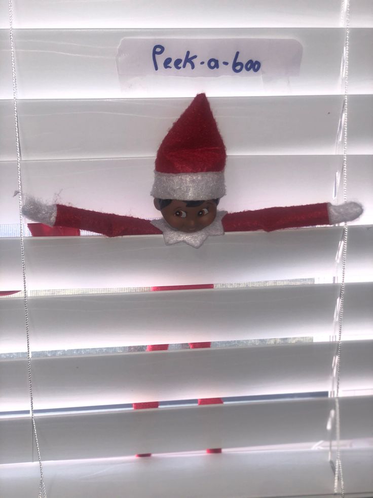 an elf peeking out from behind blinds with the words peek - a - boo on it