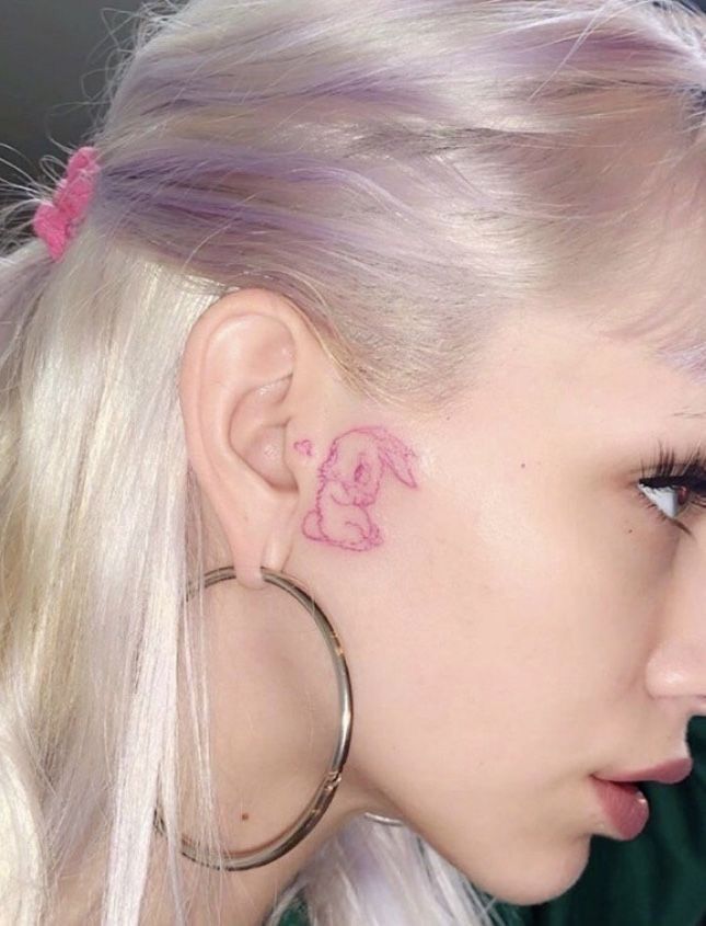 a woman with pink ink on her left ear and behind her ear is an elephant