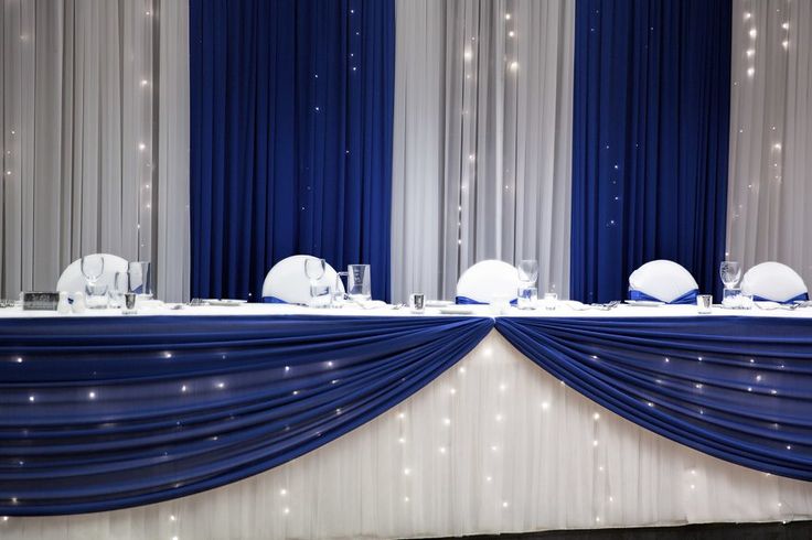 the table is set up with white plates and silver napkins on it, along with blue drapes