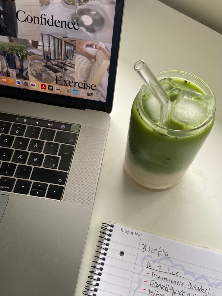 an open laptop computer sitting on top of a desk next to a cup of green liquid