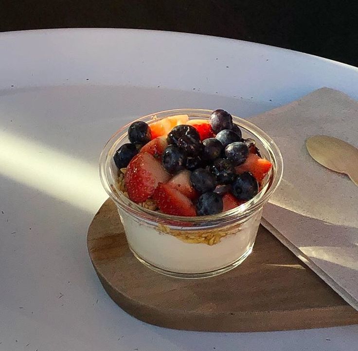 a glass bowl filled with fruit on top of a white plate next to a spoon