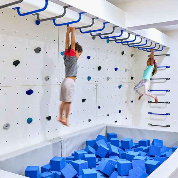 two children are climbing on a rock wall with blue blocks in the foreground and one child is jumping