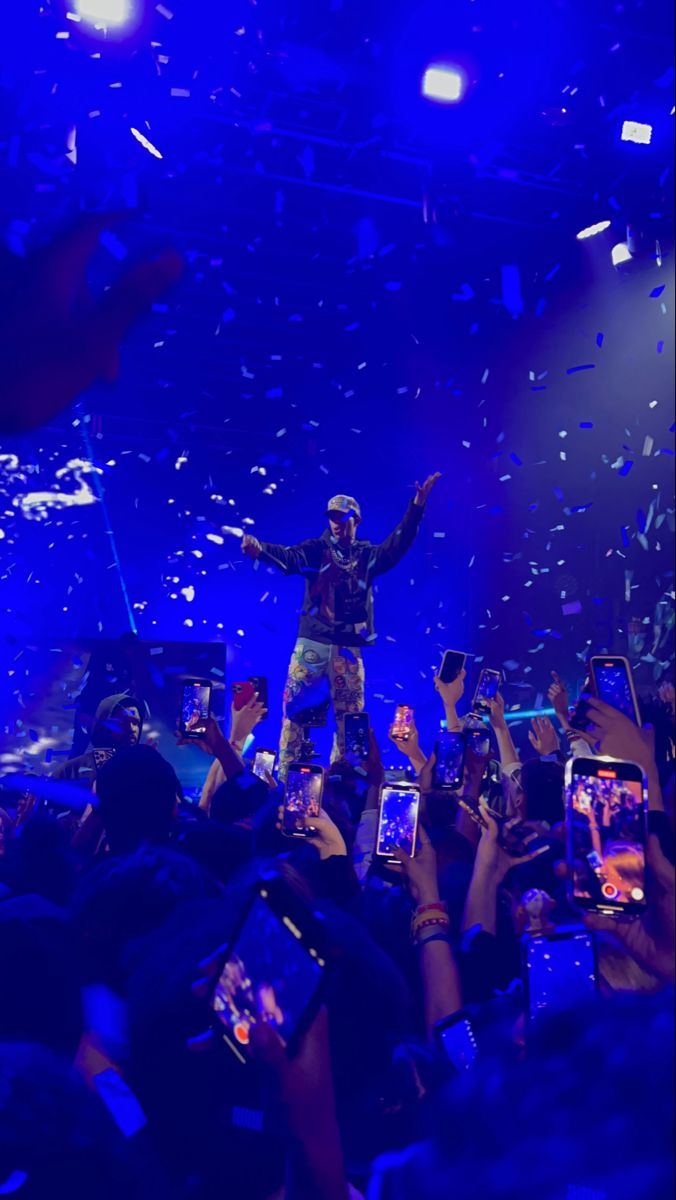 a man standing on top of a stage surrounded by people holding up their cell phones