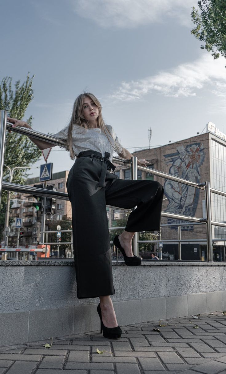 a woman leaning on a rail with her legs crossed and wearing high heels, posing for the camera