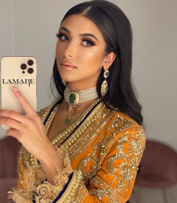 a woman holding up a cell phone in front of her face and wearing an elaborate outfit