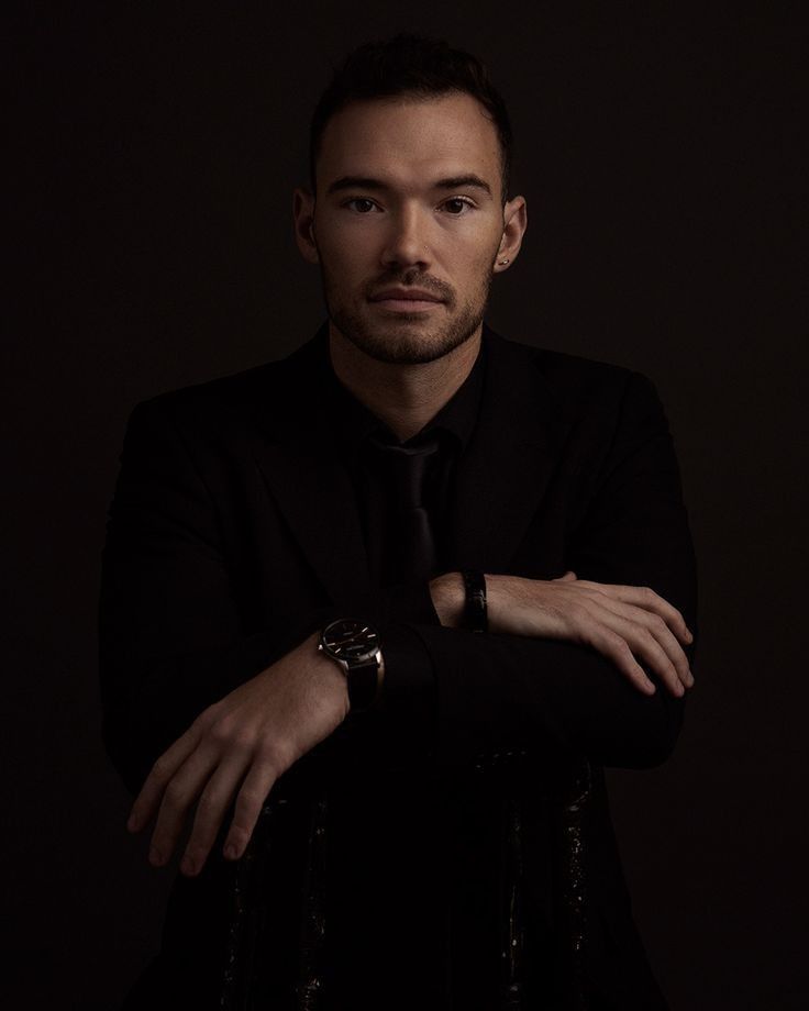 a man in a black suit and tie with his arms crossed looking at the camera