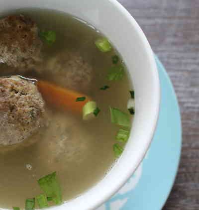 a white bowl filled with meatball soup on top of a blue and white plate