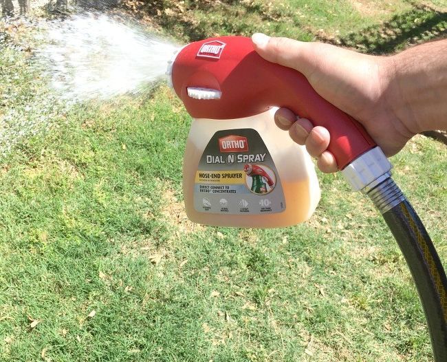 a hand is holding a sprayer and spraying water on the grass in front of a fire hydrant