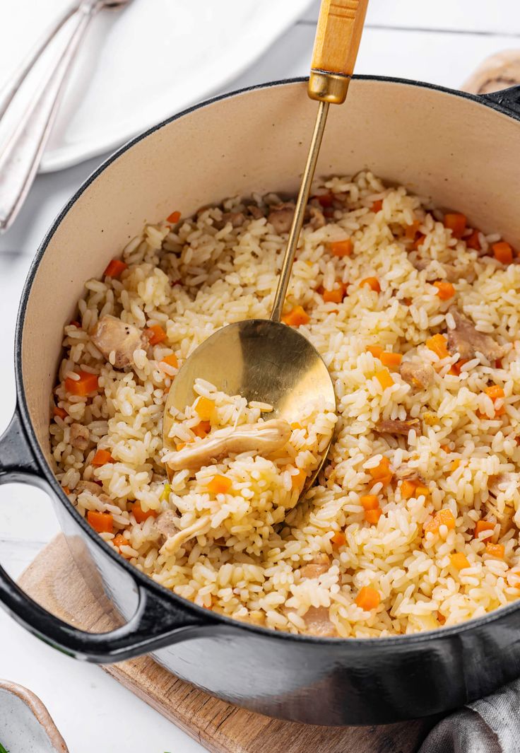 a pot filled with rice and vegetables on top of a wooden cutting board next to utensils